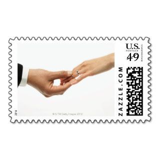 Man placing wedding band on woman's hand (focus postage stamp